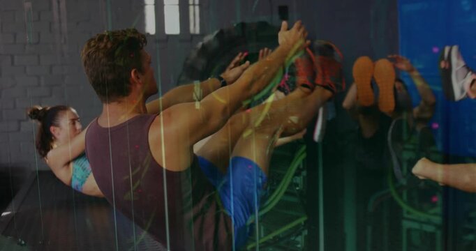 Leader in purple tank initiating V-sit core exercise on gym mats while group following for fitness