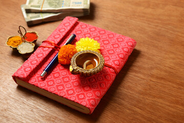 Diwali Pooja ritual. A traditional account book which is used by Indian traders worshiped during Diwali Puja. Red color account book and pen placed with Diya, flowers and currency notes.