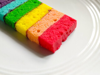 Colorful rainbow sponge cake slice served on a white plate.