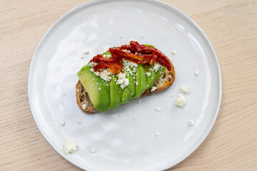 A plate of avocado toast with feta cheese and sundried tomato.