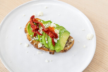 A plate of avocado toast with feta cheese and sundried tomato.