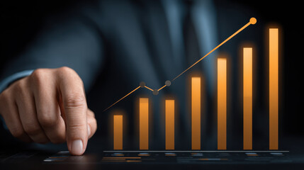 Business person pointing at glowing orange rising bar graph showing growth and success in dark background with suit and tie
