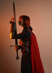 portrait of Fantasy warrior woman model, holding sword weapon, historical medieval armour costume with red fairytale cloak, strong fantasy knight. side profile pose on golden studio background.