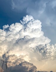 A towering cumulus cloud dominates a vast blue sky, illuminated from within, showcasing its texture and depth