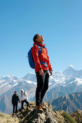Hiker standing on rocky peak under clear blue sky with snowy mountains and companions in the background, Generative AI