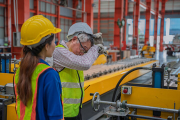 Exhausted senior factory worker wiping sweat while working on production line with colleague. Industrial teamwork, manufacturing effort, and workplace fatigue concept.