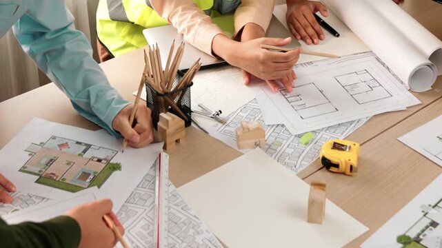 Smart architect and safety engineer discussion about building blueprint on table with architectural document, measurement tools and wooden block scatter around at modern office. Closeup. Delineation.