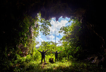 The silhouette of two adventurers celebrating at the mouth of Batu Aji Karst Cave in East Kutai, East Kalimantan, Indonesia. A triumphant moment capturing the spirit of exploration and caving