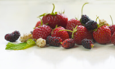 There are white and red mulberries and strawberries on the table.