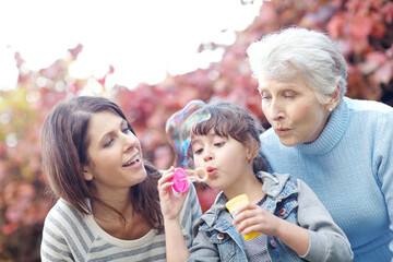Grandmother, child and blowing bubbles with mom outdoor for play, bonding and care with bokeh. Park, family and girl with soap toy for game, grandparent and mother with happy generations together