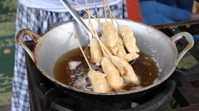 Street vendor frying traditional Indonesian snack called sempol. Sempol is a skewered and seasoned chicken-based snack, deep-fried until golden brown, commonly sold by street food vendors in Indonesia