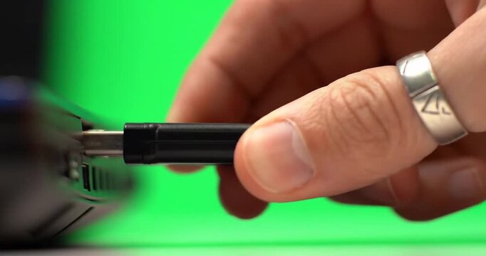 Hand inserting USB drive into laptop on green backdrop