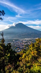 Panoramic view of a town nestled at the base of a volcano, with pine trees framing the scene