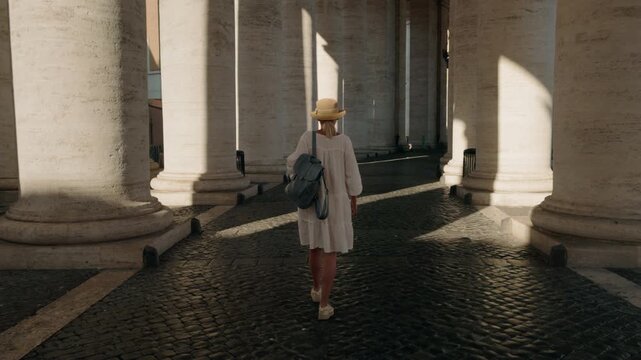 Young woman walking under colonnade in Vatican City at sunrise