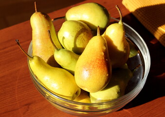 Ripe yellow-green pears in a transparent glass bowl on the table.