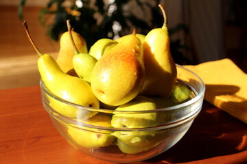 Ripe yellow-green pears in a transparent glass bowl on the table.