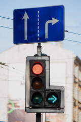 Urban traffic light with red and green signals under blue directional road sign showing straight...