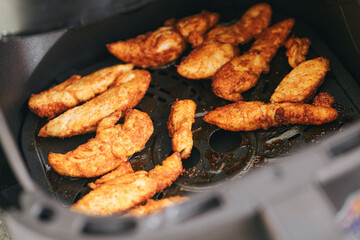 Cooked chicken strips in air fryer. Hot grilled poultry fillets baked with golden texture. Homemade meal preparation with healthy protein food and modern kitchen appliance for lifestyle.