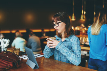 Woman, reading and tablet at table with coffee, email and notification at restaurant. Person, digital app and remote work at cafe with mug, technology and internet connection for communication.