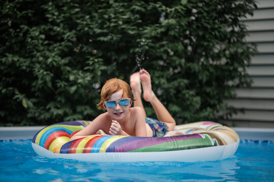 Cool boy in trendy sunglasses smiling while laying on raft
