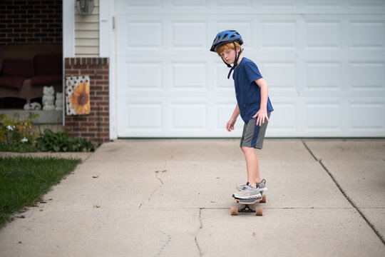 Young boy skateboarding safely with helmet on driveway pavement