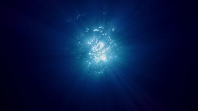 Bottom-up view on dancing sunbeams play in depth ocean. Underwater scene, sunlight from blue abyss, Slow motion of sunshine filters down through blue water. Sun rays shine under ripples water surface