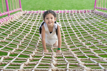 The girl is climbing the net rope in the playground.