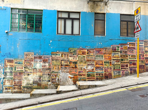 Vibrant urban street mural painted on a blue wall depicting traditional Hong Kong residential tenement buildings along a sloped street in Central district with traffic sign. graham street old central