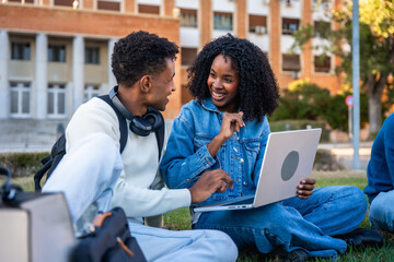 Students collaborating on laptop, smiling in university campus