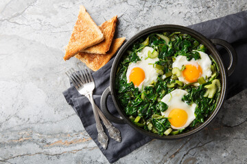 green shakshuka is healthy, one-pan and full of fresh herbs, spinach, and eggs closeup on the pan on the table. Horizontal top view from above