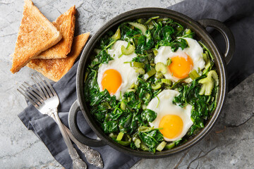 Green shakshuka is a stew of eggs in a mixture of green vegetables and herbs, close-up in a frying pan on a table. Horizontal top view from above