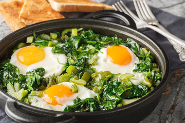 Green shakshuka one-pan dish filled with shaved spinach, green pepper, celery and herbs closeup on the pan on the table. Horizontal