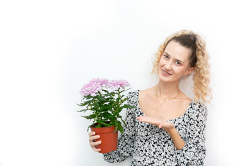 Cheerful woman in floral dress holding and showing a pot with pink chrysanthemums, concept of gardening
