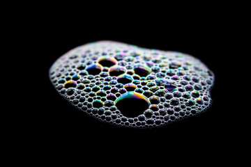 Iridescent soap bubbles cluster on a black background with glittering hues.