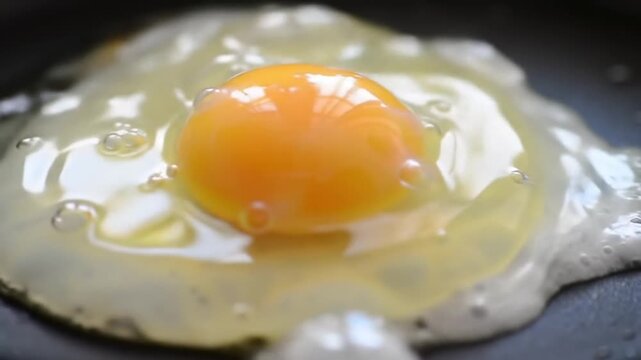 Macro Extreme Close Up of Egg Cracking Open onto a Black Surface Yolk Spreading and Sizzling on a Frying Pan with Bright Interior Light For Culinary Preparation and Background