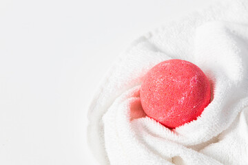 Red bath bomb resting on a white towel for a relaxing spa experience at home