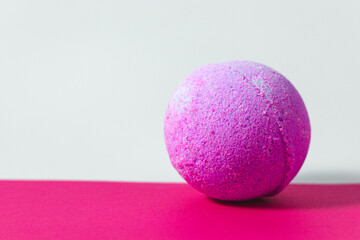 Bright purple bath bomb resting on a pink surface in a relaxing setting
