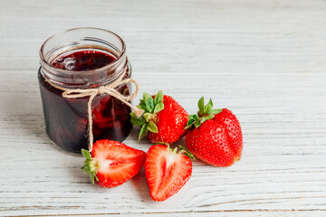 Delicious strawberry jam beside fresh strawberries on wooden table