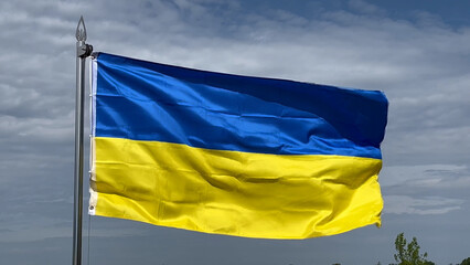 Large yellow and blue flag of Ukraine waves against the cloudy sky. National state symbol of Ukraine.