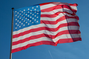 American flag waving in the wind against a clear blue sky, showcasing vibrant colors and intricate details, symbolizing patriotism and national pride