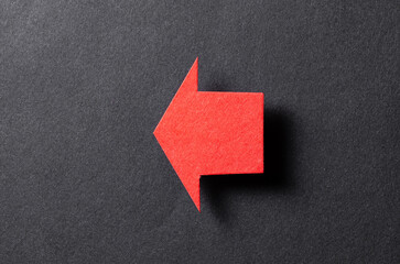 Red blank paper cardboard arrow direction sign with shadow and copy space for text on black background, flat lay top view pointing symbol conceptual message backdrop