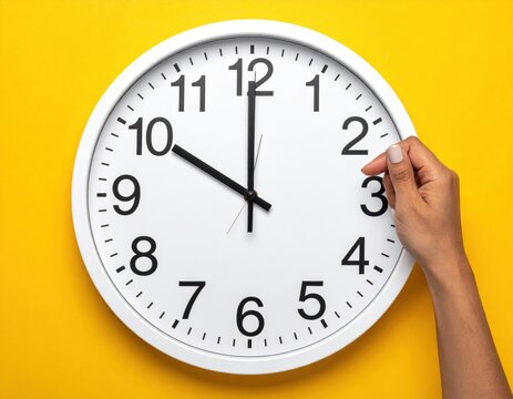 Hand adjusting a white clock on a yellow background, showing 10 o'clock.