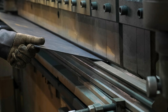Factory worker bending metal sheet using press brake machine in workshop. Metalworking metallurgical industry, automated machinery production manufacturing. Working in plant floor with details, parts.