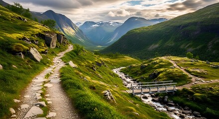 Fototapeta premium A stunning, lush green valley in the Norwegian mountains. A winding stone hiking path leads past a rushing river and a small bridge, set beneath a dramatic, cloudy sky