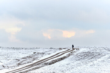 A lonely man on a snowy country road in a field against a cold sky