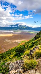 Panoramic vista of a high-elevation valley, with rocky, grassy slopes and a mountain range in the background