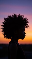 Fototapeta premium Silhouette of a young African-American woman with curly hair against a bright sunset sky. World Afro Day, September 15