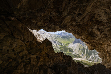 A breathtaking view of the mountain meadow Korošica through a natural rock window on Najvišji rob in the Kamnik-Savinja Alps, Slovenia.