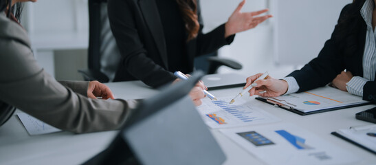Business women collaborating and discussing financial reports with charts and graphs, pointing at key metrics while working together on a strategy in a modern office