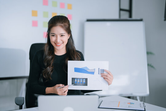 Businesswoman explaining charts and graphs on a document during a virtual meeting, communicating financial analysis and business strategy from a modern office workspace